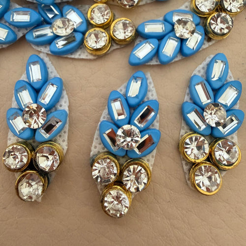 Hand holding a blue rhinestone leaf patch to show size
