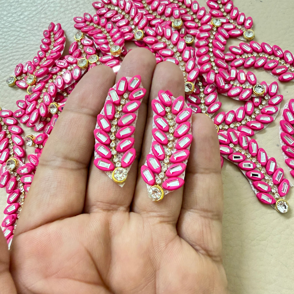 Multiple hot pink rhinestone leaf motif patches held in hand showing size