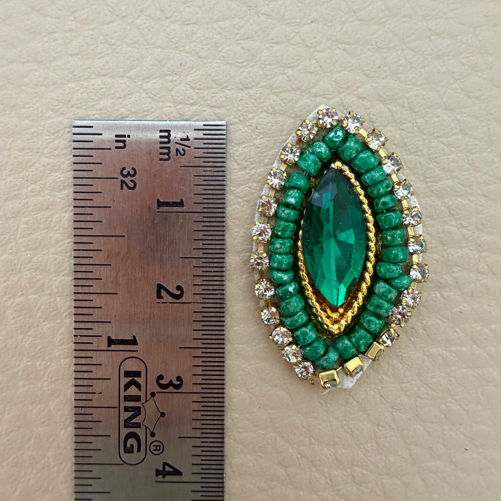 Close-up of emerald green crystal patch with clear rhinestone border, green beads, and gold-tone accents