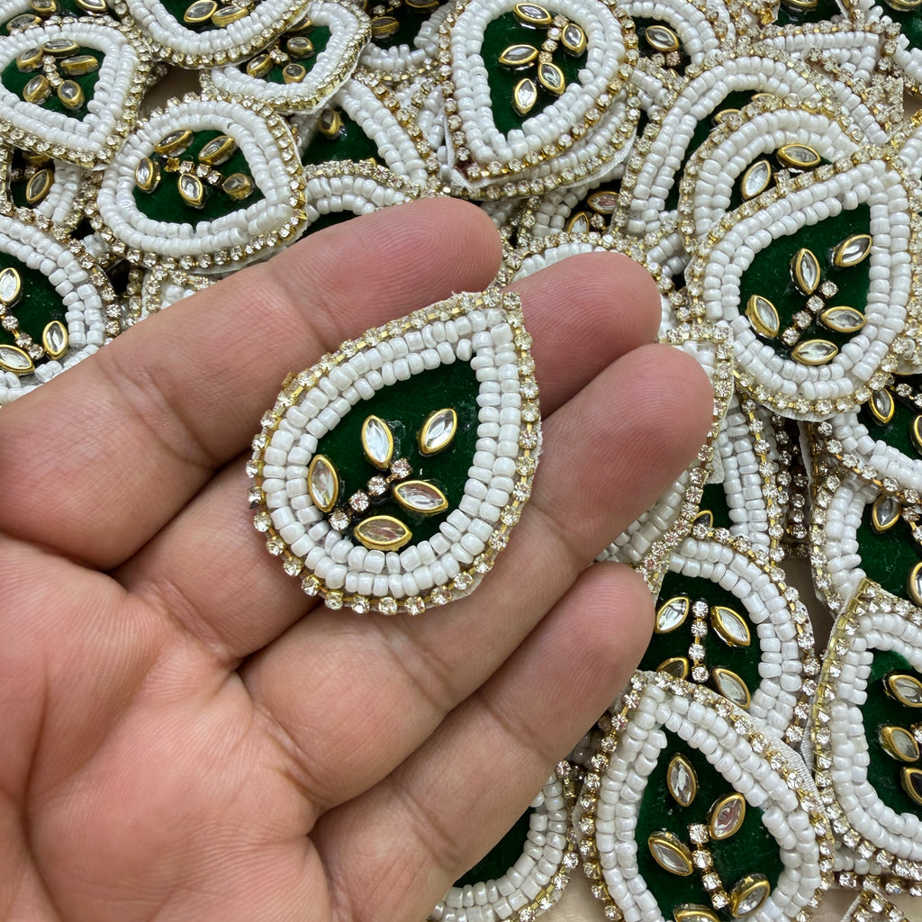 Close-up of two bottle green kundan teardrop patches with white beads