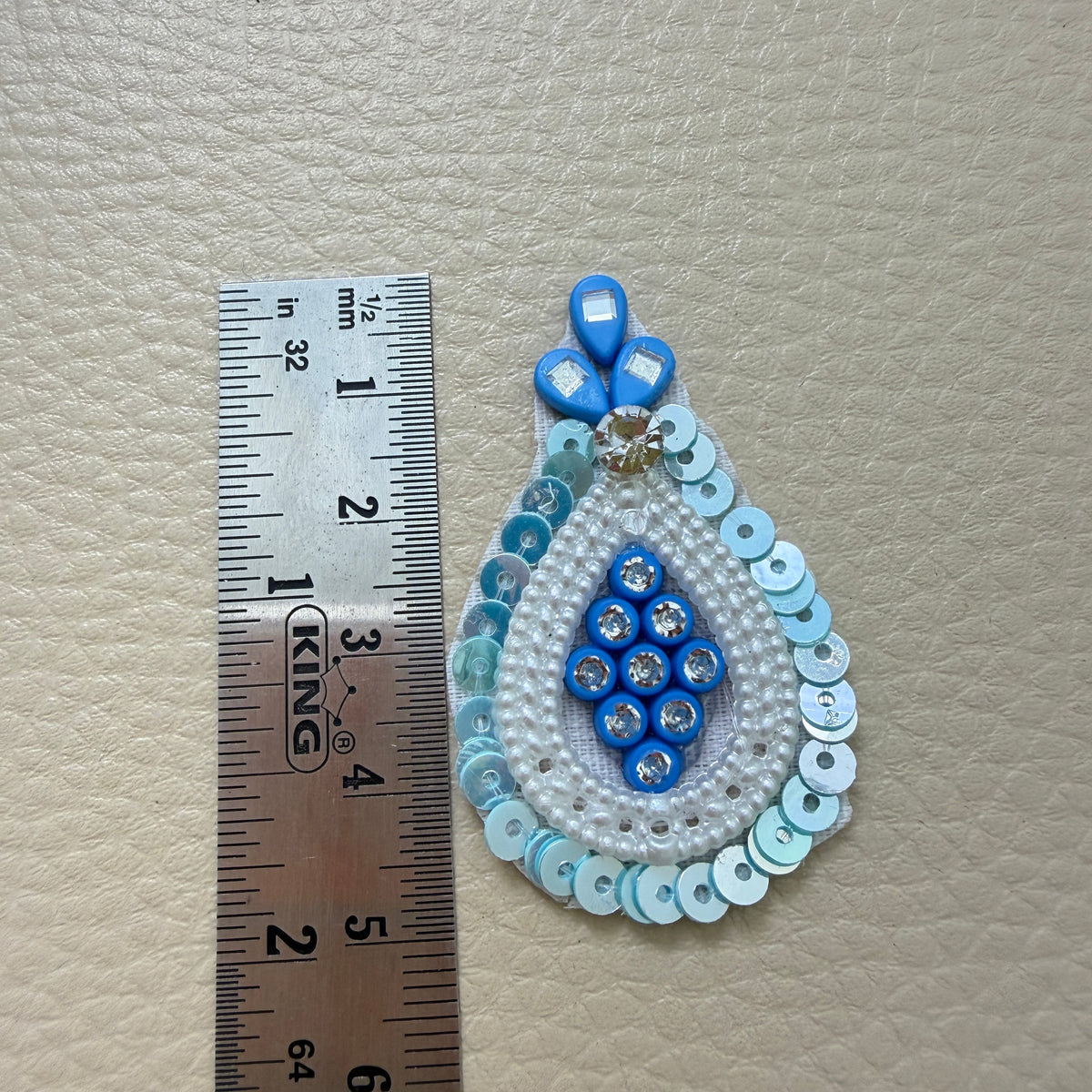 Blue teardrop applique patch held in a hand for scale