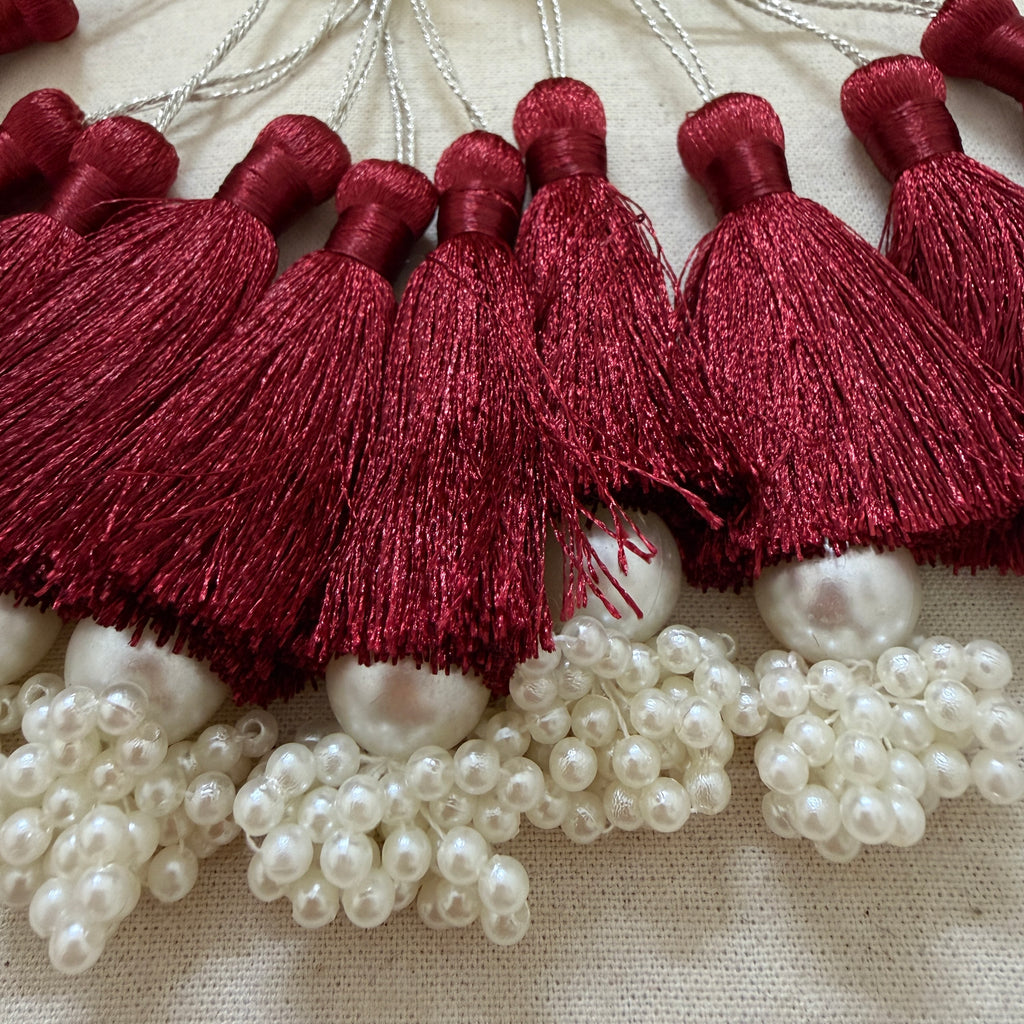 Multiple maroon silk tassels with pearl cluster base laid flat showing full collection