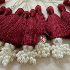 Multiple maroon silk tassels with pearl cluster base laid flat showing full collection