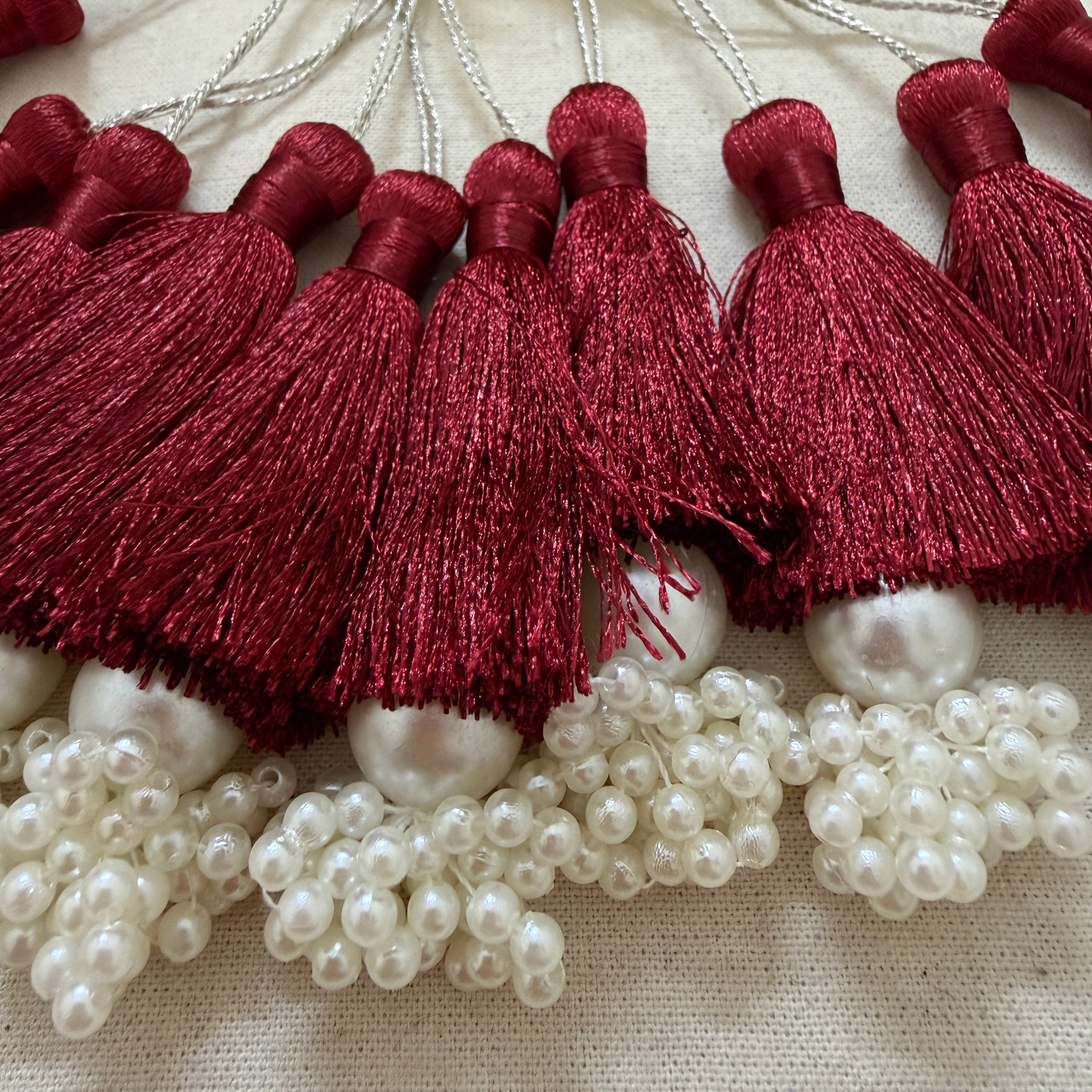 Multiple maroon silk tassels with pearl cluster base laid flat showing full collection