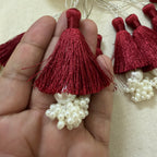 Single maroon silk tassel with pearl cluster held in hand showing size