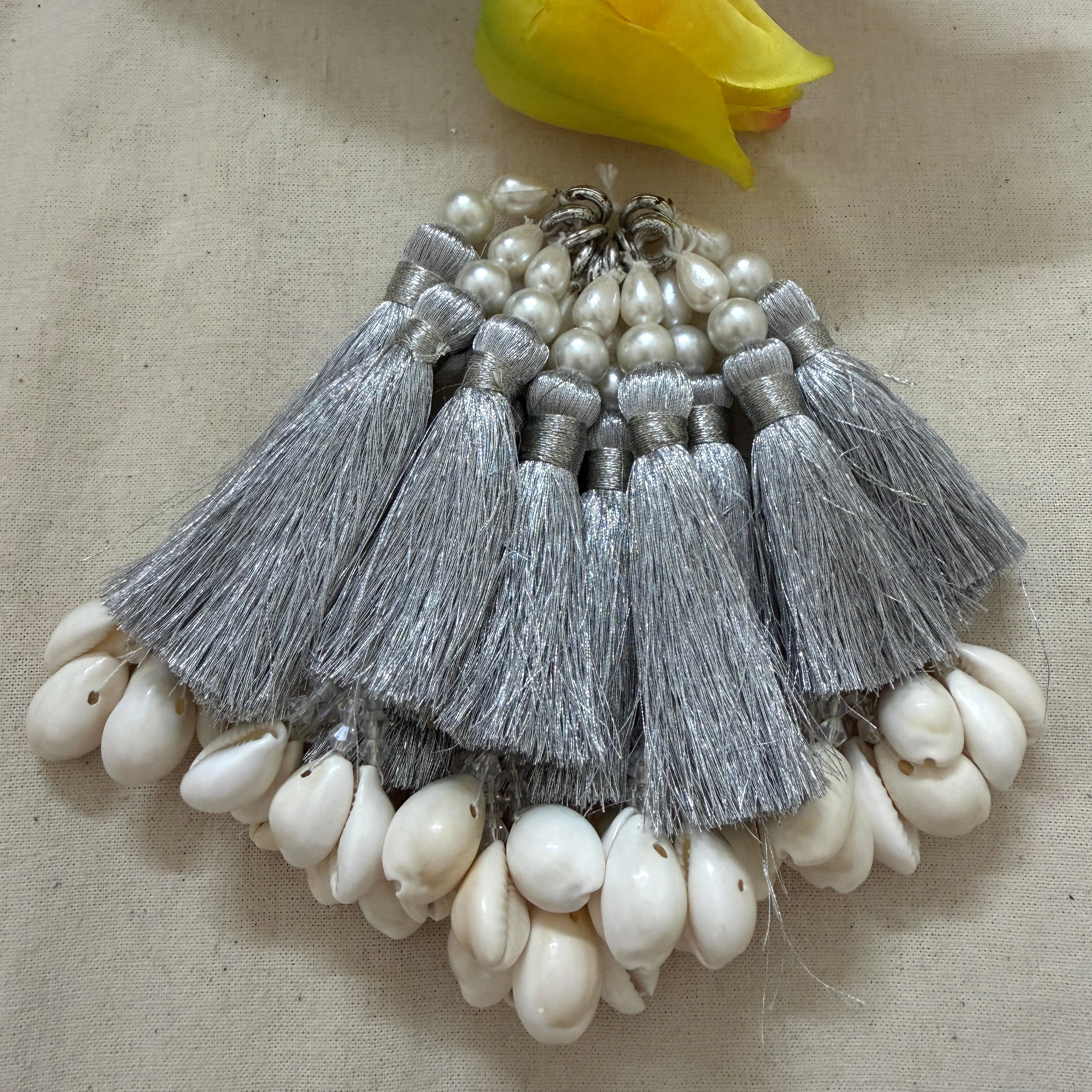 Multiple silver silk tassels with cowrie shells fanned out on fabric