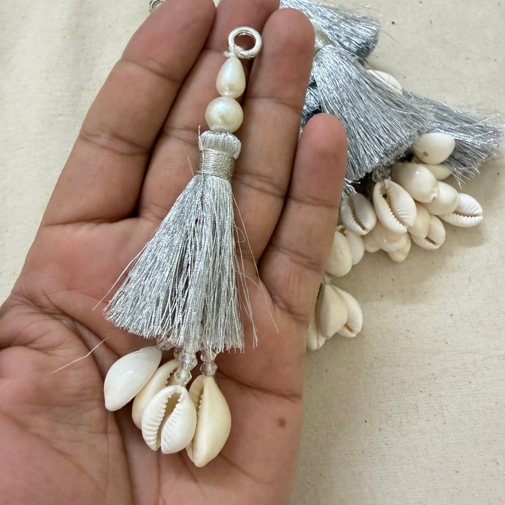Single silver silk tassel with cowrie shells and pearl beads held in hand showing size