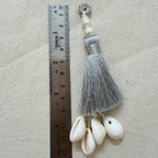 Single silver silk tassel with cowrie shells next to ruler showing approx 12cm length
