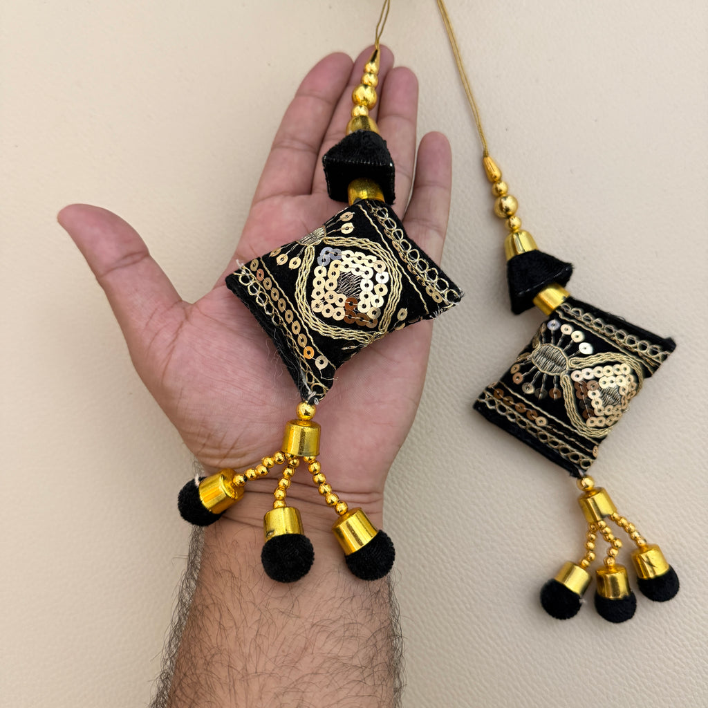 Black and gold embroidered tassel pair beside a ruler for size reference