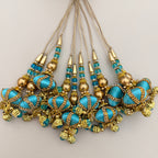 Turquoise and gold-tone latkan tassel shown on a hand for scale