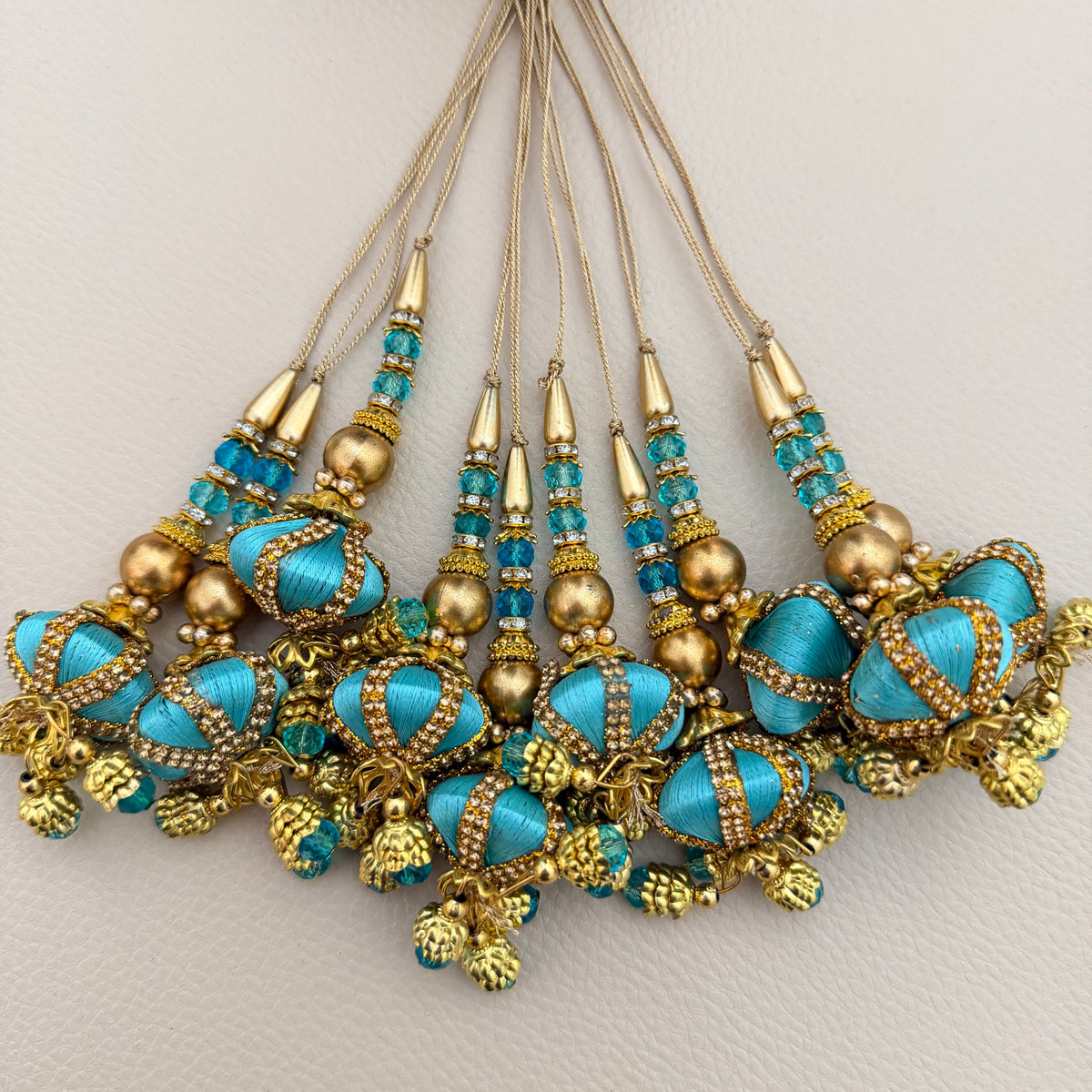 Turquoise and gold-tone latkan tassel shown on a hand for scale