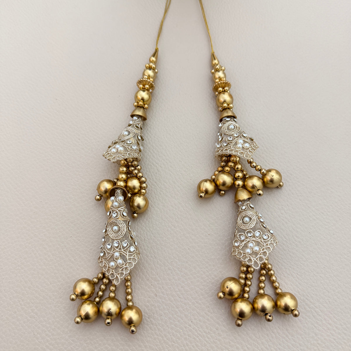 Gold-tone double-tier latkan tassel displayed on a hand for scale