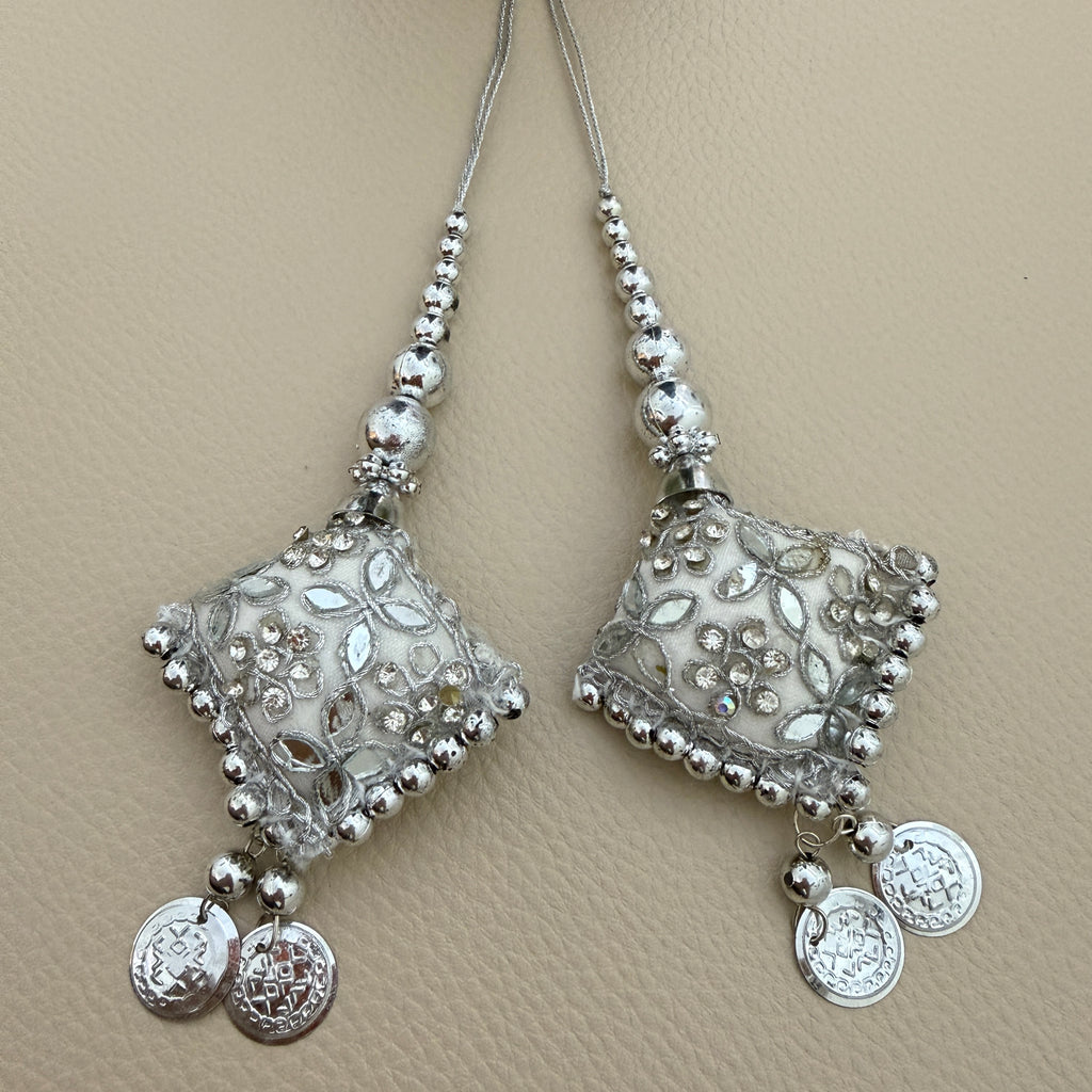 Pair of silver and white diamond-shaped latkan tassels with floral embellishments, beaded cords and dangling coin charms