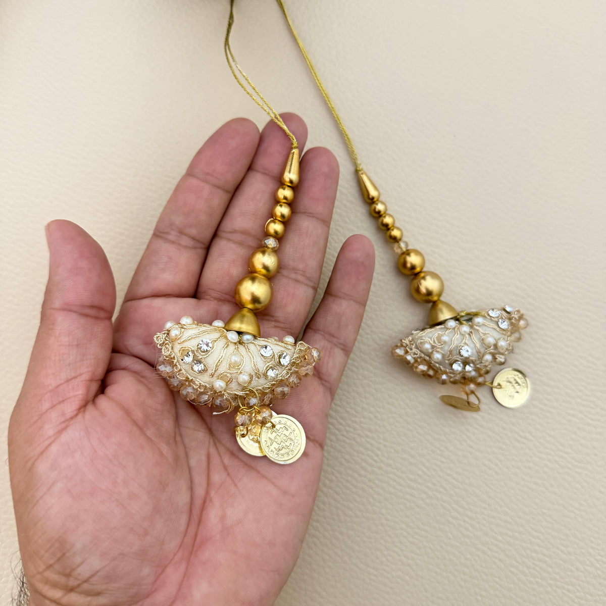 Ivory and gold umbrella latkan tassel held in a hand showing decorative beadwork and coin charms