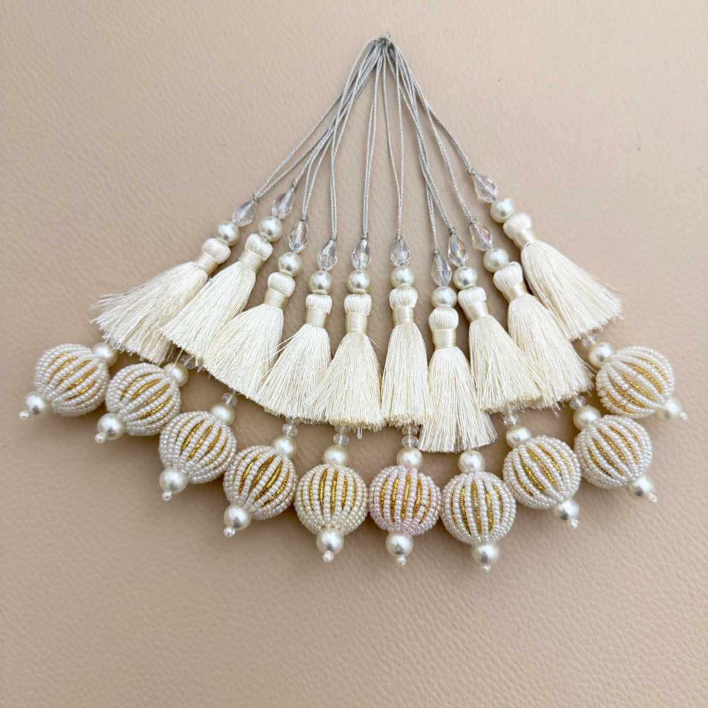 Ivory thread tassel held in a hand showing pearl-look beads and gold-tone details on the round pendant