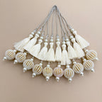 Ivory thread tassel held in a hand showing pearl-look beads and gold-tone details on the round pendant