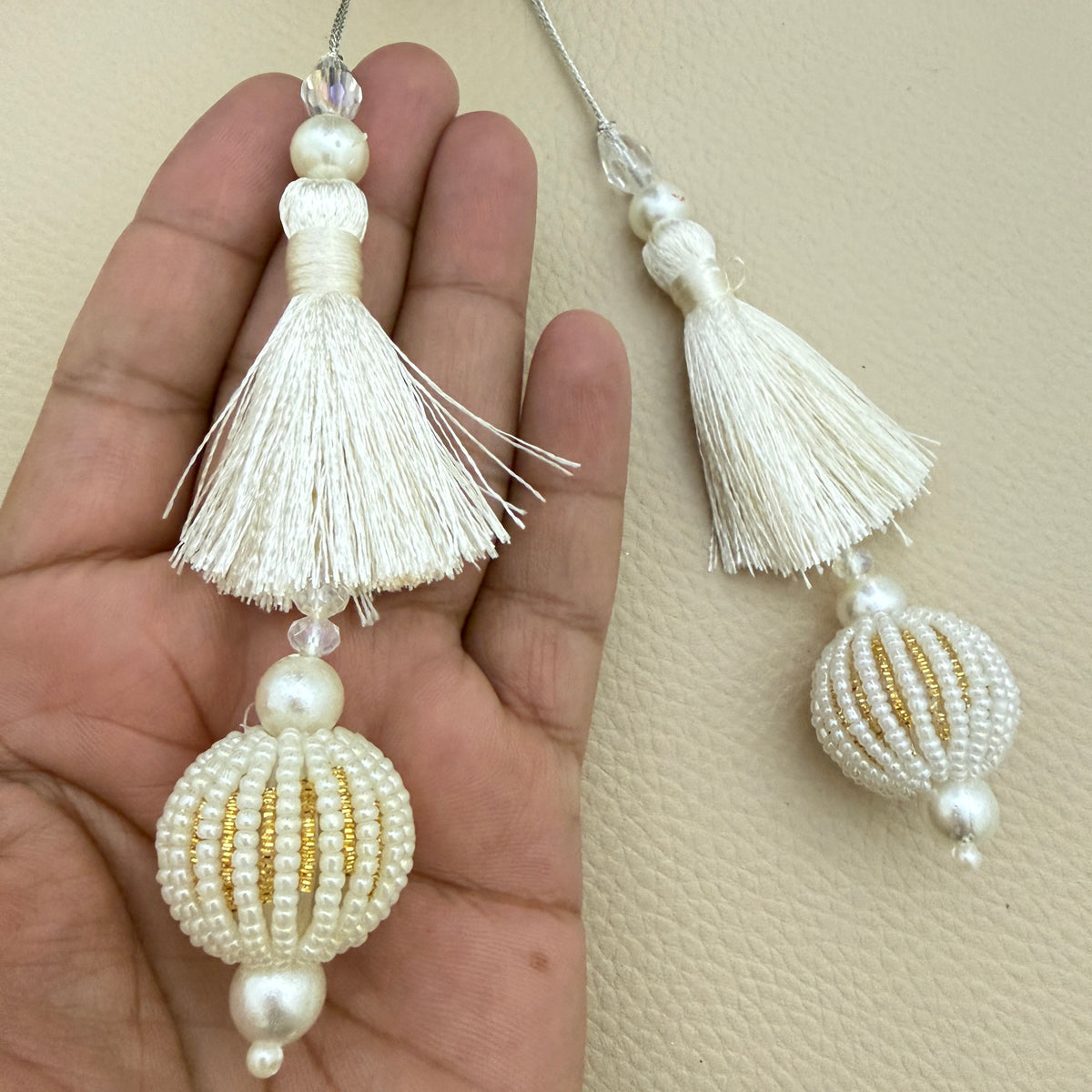 Two ivory beaded ball latkan tassels beside a ruler for size reference