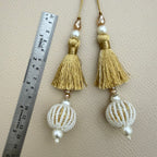 Gold thread latkan tassel held in a hand showing white beaded ball and champagne-coloured accents