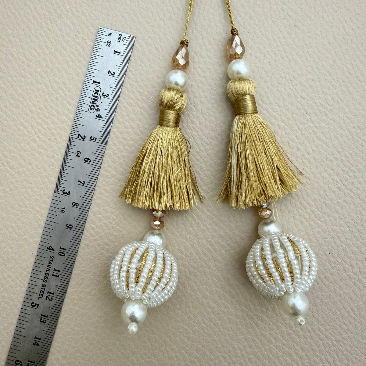 Gold thread latkan tassel held in a hand showing white beaded ball and champagne-coloured accents