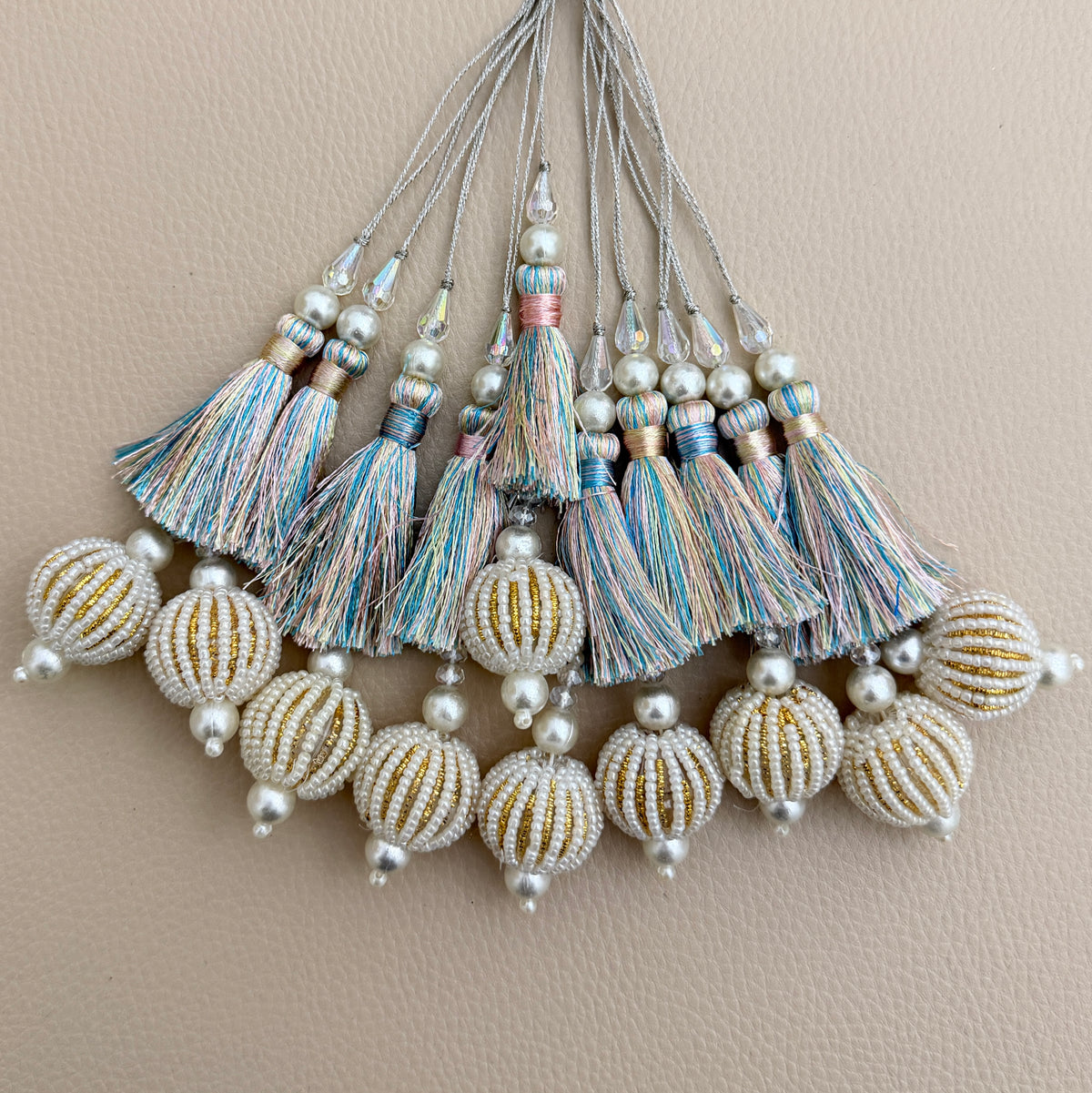 Pastel multicolour thread tassel held in a hand showing pearl-look beaded ball pendant