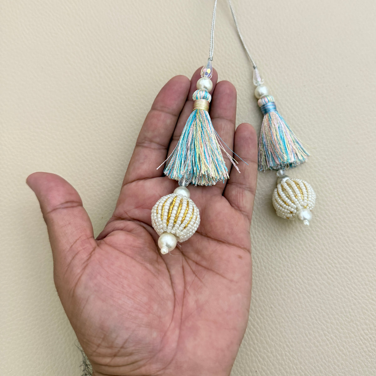 Two pastel multicolour latkan tassels beside a ruler for visual size reference