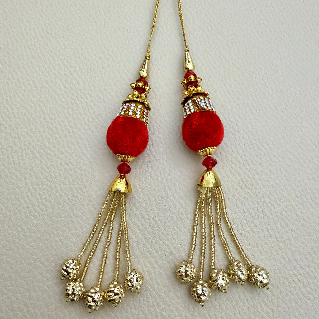 Close-up of red pom pom latkan tassel with gold-tone chains held in a hand