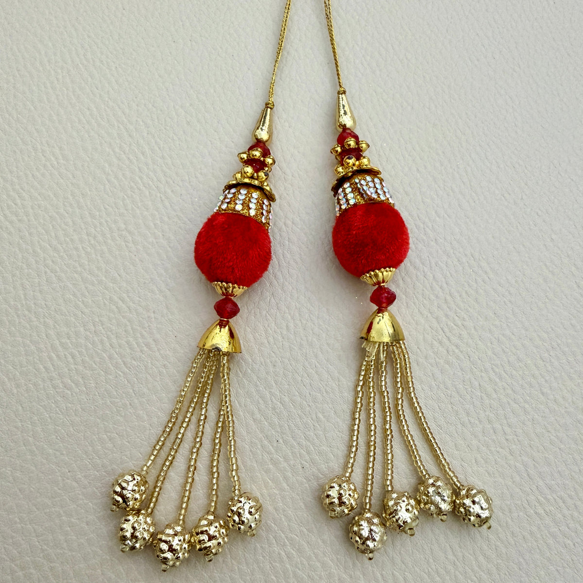 Close-up of red pom pom latkan tassel with gold-tone chains held in a hand