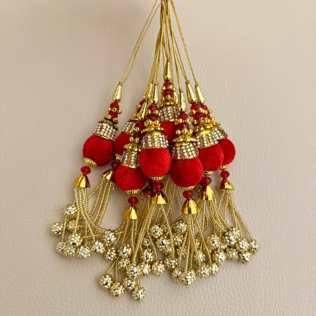 Red and gold-tone latkan tassel beside a ruler for size reference